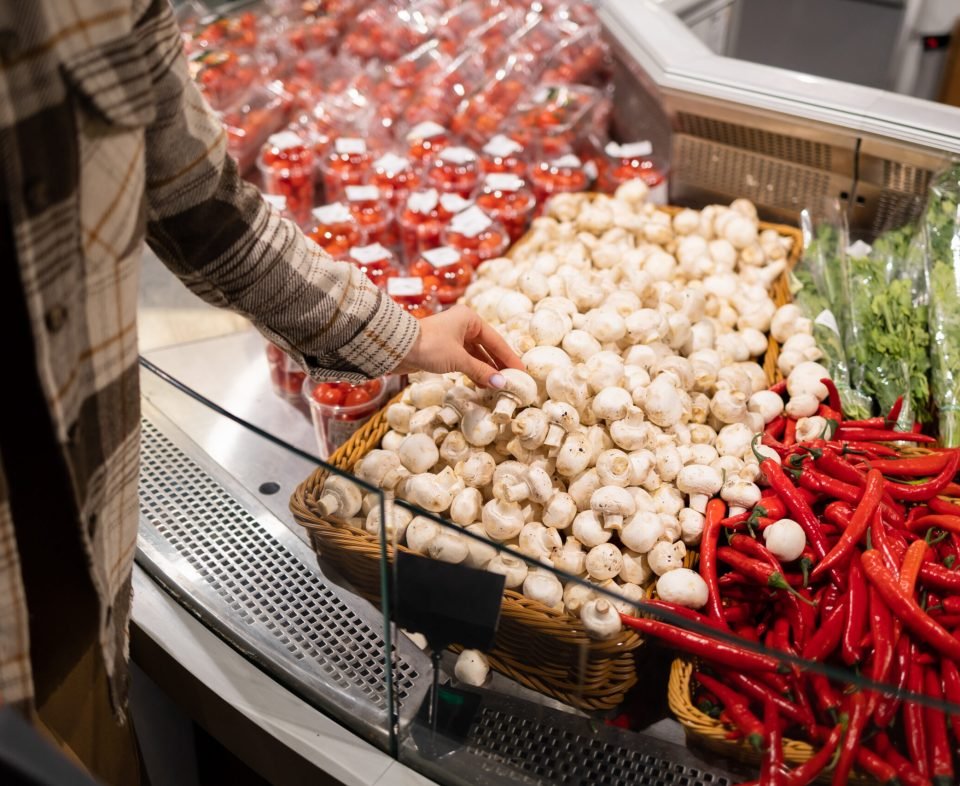 Woman chooses champignons in the vegetable section of the supermarket